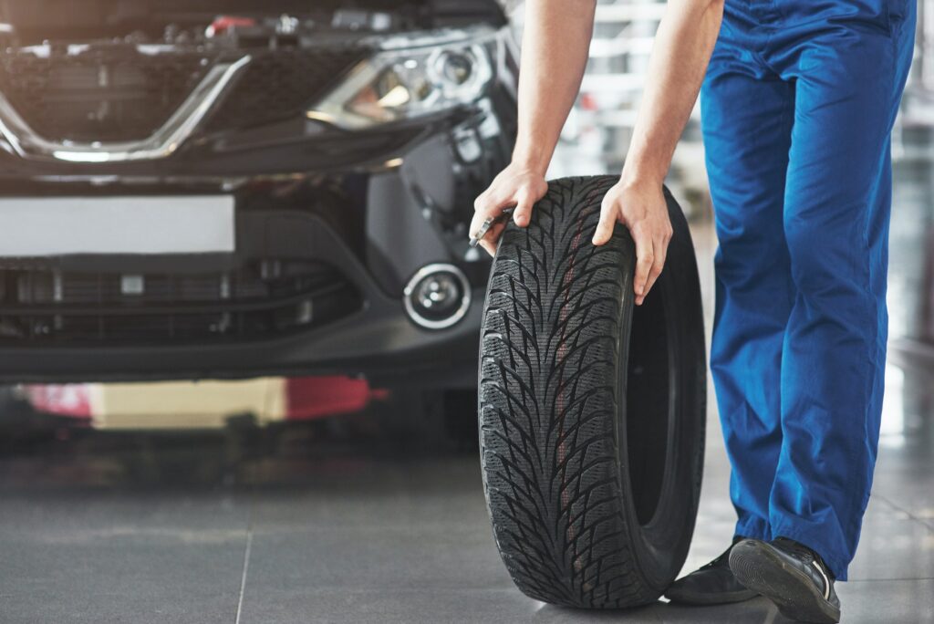 technician-with-a-blue-workwear-holding-a-wrench-and-a-tire-while-showing-thumb-up